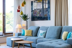 Uma sala de estar moderna com um sofá cinzento, uma mesa redonda pequena e um quadro na parede.