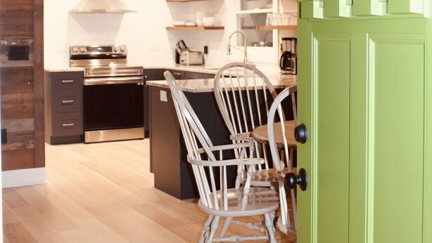 Une cuisine moderne avec des meubles en bois, un four en acier inoxydable et un coin repas agrémenté d’une chaise blanche.