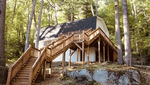 Une cabane avec un escalier en bois menant à une véranda, le tout entouré d’arbres.
