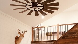 Un intérieur rustique avec un escalier en bois, une tête de cerf accrochée au mur, un grand téléviseur à écran plat, une table basse en bois et un canapé confortable.