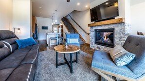 Ein modernes Wohnzimmer mit Kamin, Deckenventilator und einem darüber montierten Fernseher.