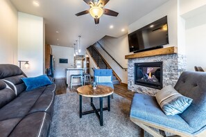 Ein modernes Wohnzimmer mit Kamin, Deckenventilator und einem darüber montierten Fernseher.