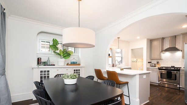 Een moderne keuken met witte kasten, een centraal eiland en een eethoek met een zwarte tafel en stoelen.