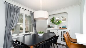 Een eetgedeelte met een zwarte tafel, vier zwarte stoelen, een witte hanglamp en een grijze gordijn.