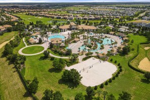 Vue aérienne d’un quartier résidentiel avec une piscine centrale, plusieurs maisons et des pelouses bien entretenues.