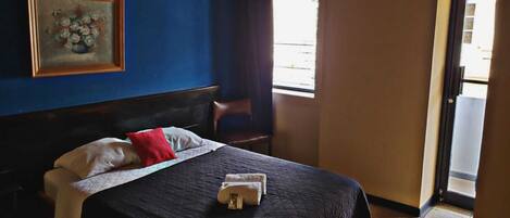 Una habitación de hotel con una cama, un cuadro en la pared y una ventana con cortinas.