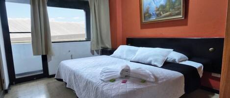 A hotel room with a bed, a painting on the wall, and a window with curtains.
