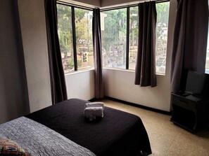 A hotel room with a bed, a TV, and large windows with curtains. - Hotel Alajuela (Alajuela)