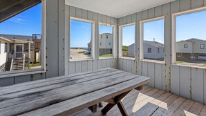 Huone, jossa on puinen pöytä ja suuret ikkunat, joista avautuu näkymä rannalle ja muihin rakennuksiin.