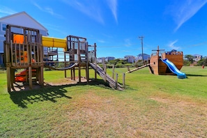Un parque infantil con un tobogán de madera y estructuras para escalar, frente a un cielo despejado.