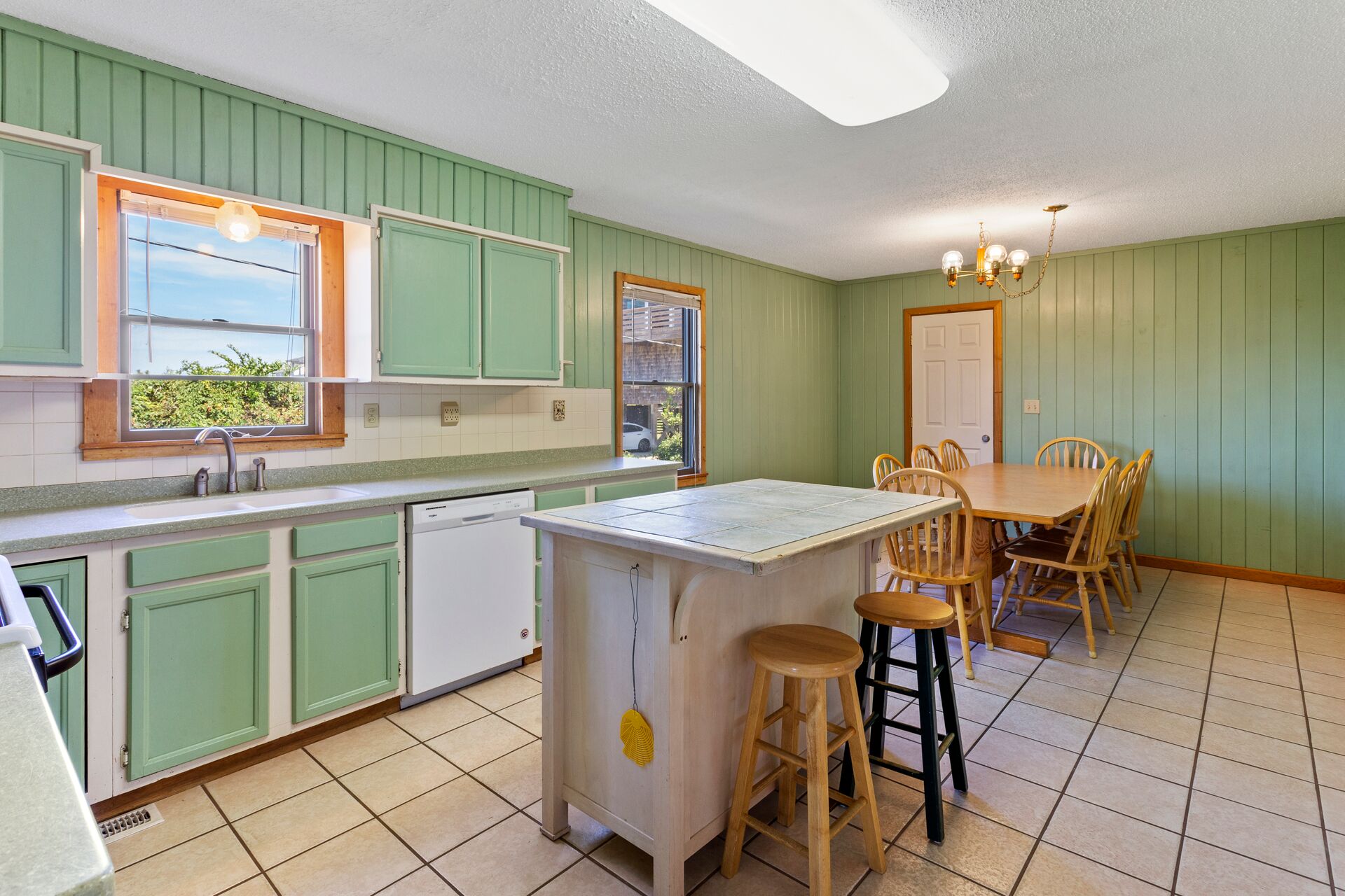 A kitchen with green cabinets, a white island, and a dining area with wooden chairs.