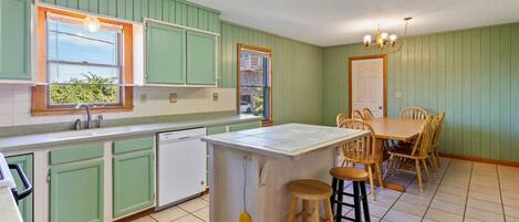 A kitchen with green cabinets, a white island, and a dining area with wooden chairs.