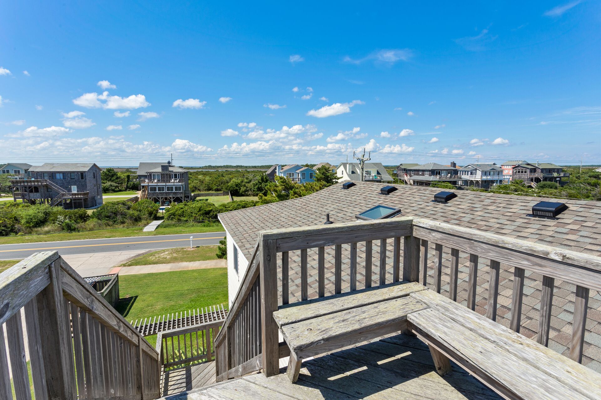 A wooden deck with a view of a residential area, including houses and a road.