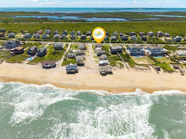 Vue aérienne d’une zone résidentielle côtière, avec des maisons, une plage et l’océan.