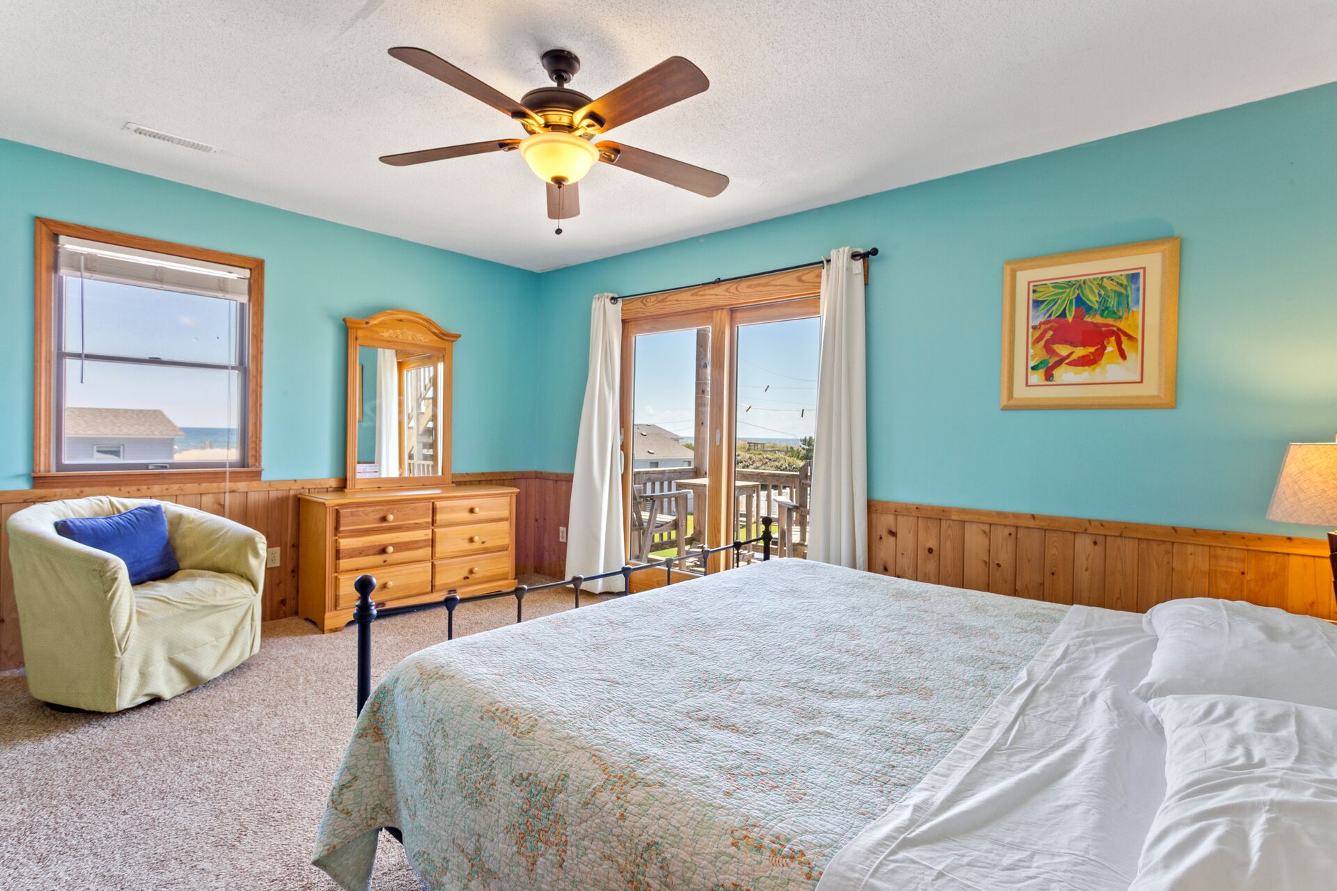 Une chambre à coucher comprenant un lit, une commode, une chaise, un ventilateur de plafond, une fenêtre et une porte donnant sur un balcon.