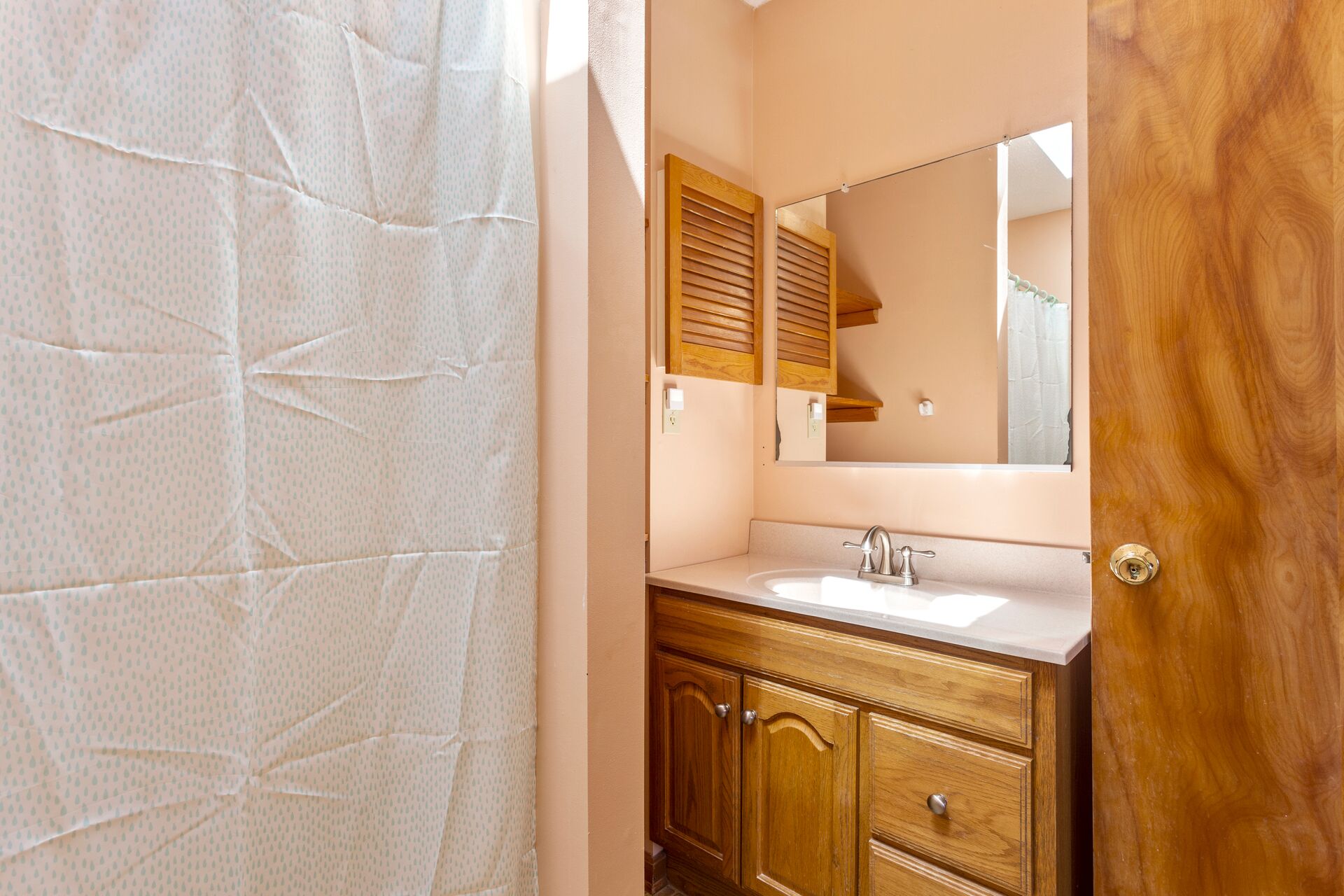 A bathroom with a wooden vanity, a mirror, and a shower curtain.