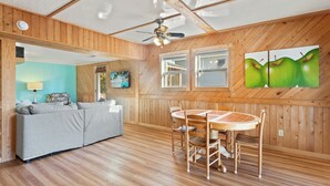A room with a wooden ceiling, a ceiling fan, a gray sofa, a dining table with chairs, and a painting of green apples on the wall. - Beach, Sunrise, Views, community pool! (Nags Head)