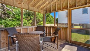 A covered outdoor area with wooden furniture, large windows, and a view of a house. - Beach, Sunrise, Views, community pool! (Nags Head)
