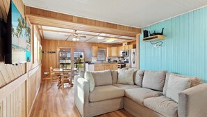 A cozy living room with a sectional sofa, wooden flooring, and a kitchen area with wooden cabinets and a microwave. - Beach, Sunrise, Views, community pool! (Nags Head)