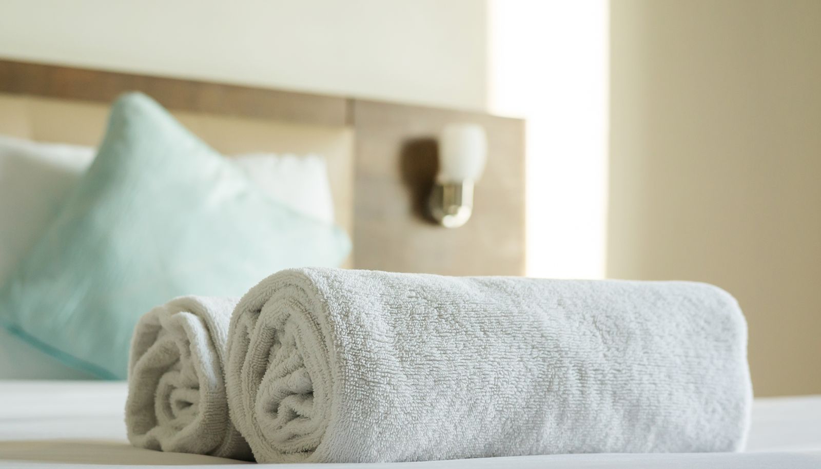 Ein ordentlich bezogenes Bett mit aufgerollten weißen Handtüchern und einem Text-Overlay mit der Aufschrift 'FREE TOWELS PROVIDED'.