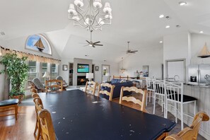 A spacious dining area with a large table and chairs, a ceiling fan, and a TV mounted above the fireplace.