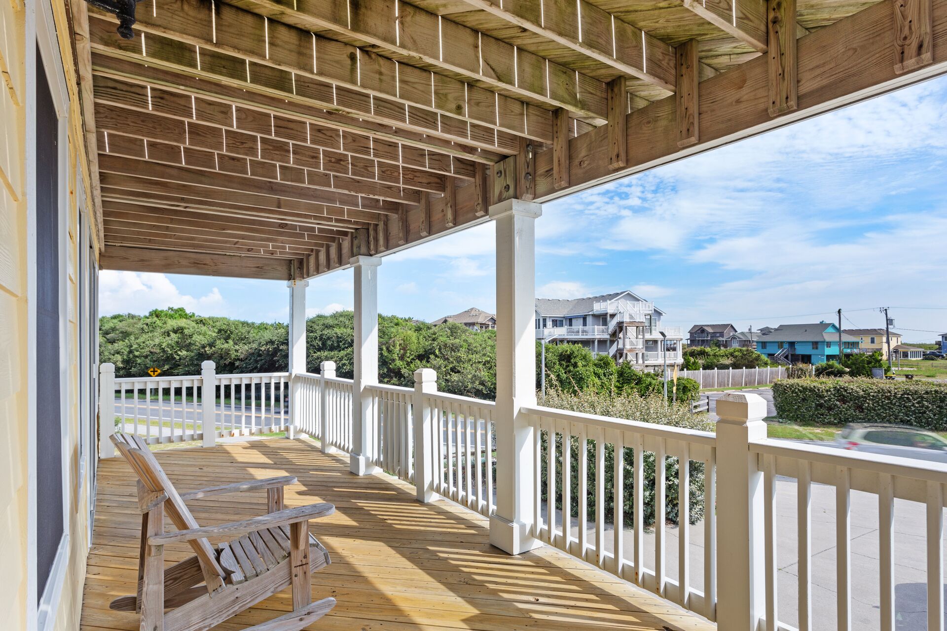 A covered wooden deck with white railings and a brick ceiling, overlooking a residential area with houses and greenery.