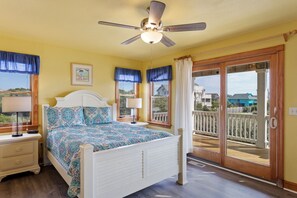 A bedroom with a bed, bedside tables, a ceiling fan, and a view of the outside.