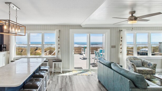 A modern kitchen with a bar area, large windows with ocean views, and a ceiling fan.