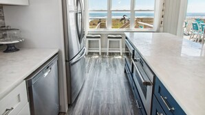 A kitchen with a view of the ocean, a refrigerator, a dishwasher, and a bar area with stools.