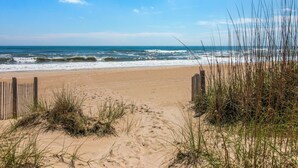 A sandy beach with a wooden fence and tall grasses in the foreground.