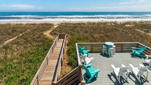 A wooden deck with chairs and tables overlooking a beach.