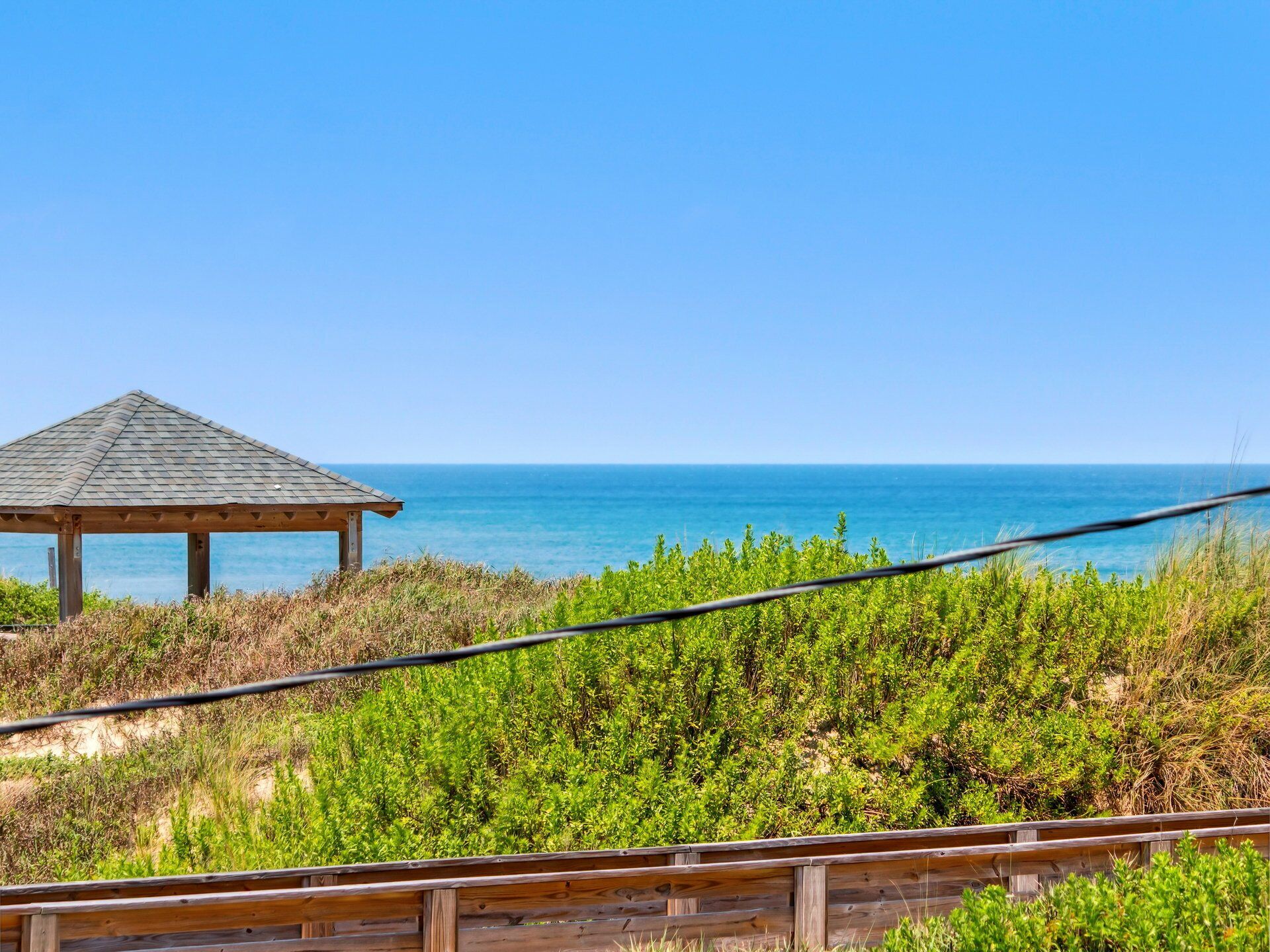 A wooden gazebo overlooking a beach with clear blue water.
