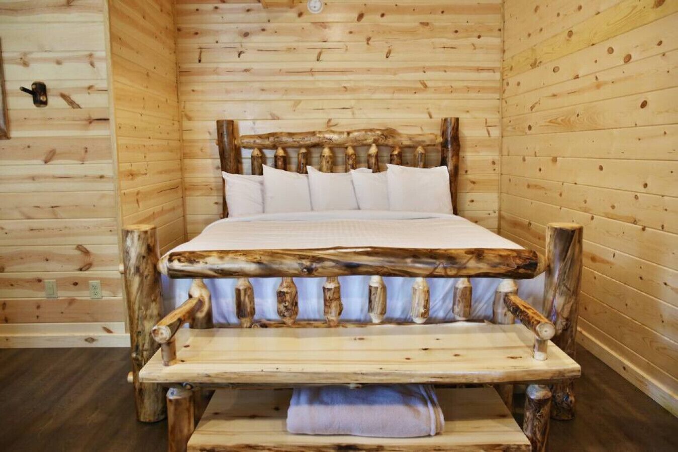 Una cama de madera con diseño rústico, con cabecera de troncos y pie cama con detalles tallados.