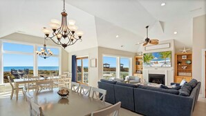 A spacious living room with a large sofa, a dining table with chairs, a fireplace, and a television. - Just Fab * Oceanfront * Elevator * Saltwater Pool * Hot Tub * Game Room * Views (Nags Head)