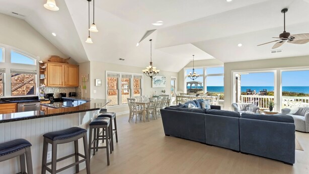 A spacious kitchen with a large island, bar stools, and a dining area with a view of the ocean. - Just Fab * Oceanfront * Elevator * Saltwater Pool * Hot Tub * Game Room * Views (Nags Head)
