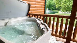 Ein Whirlpool auf einer Holzterrasse mit Blick auf einen Teich und Bäume.