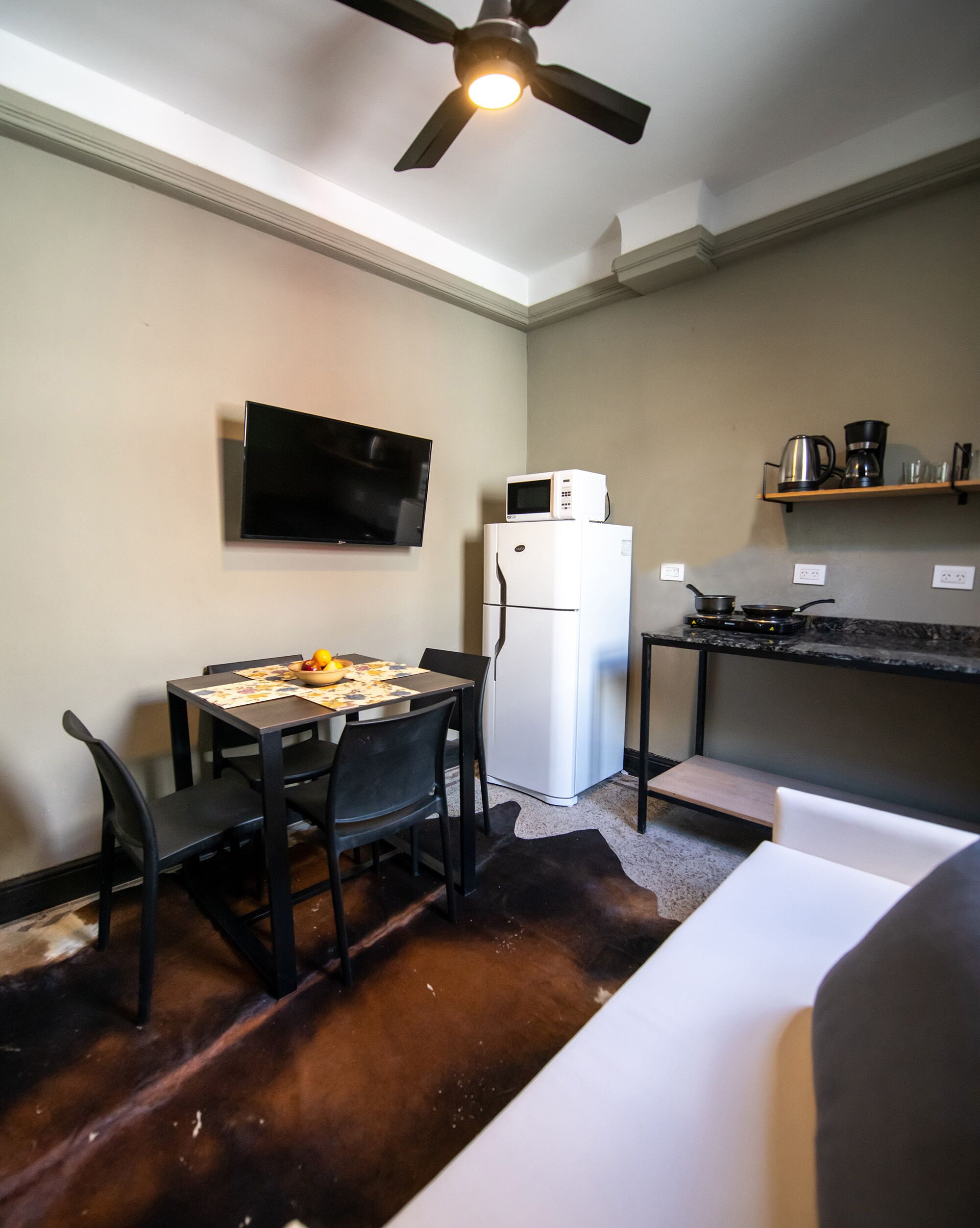 Cocina compacta con refrigerador, microondas y estufa, una mesa de comedor con sillas y un ventilador de techo.