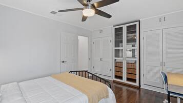 Une chambre à coucher avec un lit, un ventilateur de plafond, des armoires blanches et un bureau en bois.
