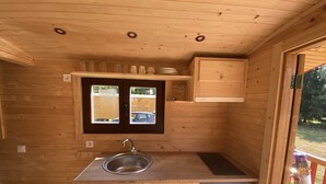 Ein gemütliches Holzhaus mit einer Küchenzeile, inklusive Spüle, Schränken und einem Fenster mit Blick ins Freie.