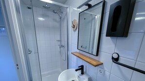 Een moderne badkamer met een douchecabine van glas, een witte wastafel met een zwarte kraan en een houten plank erboven.