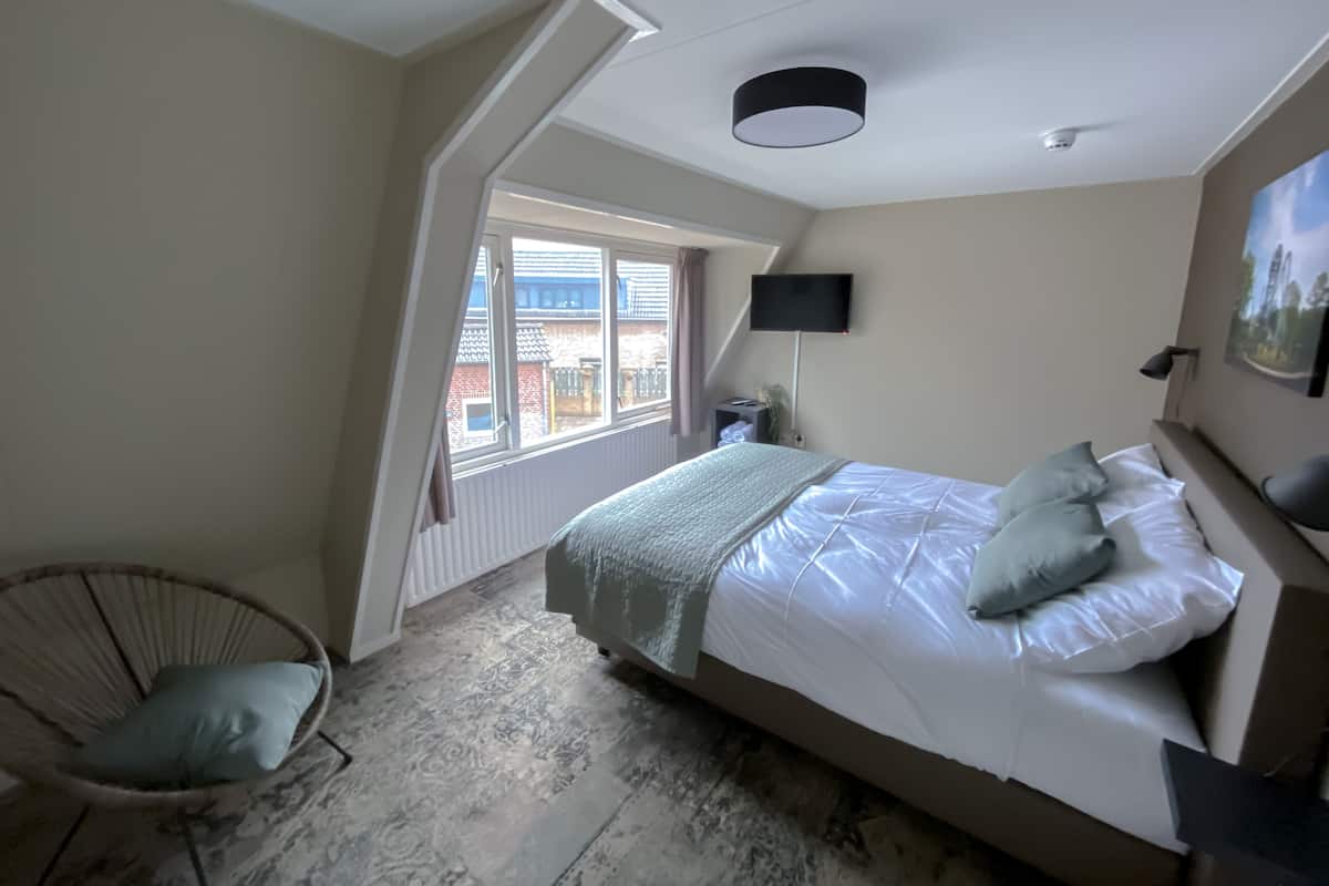 Une chambre à coucher avec un lit, une chaise, une télévision et une fenêtre.