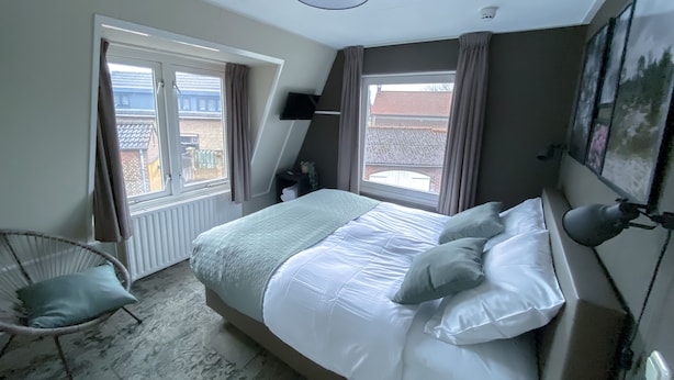 Een slaapkamer met een bed, een stoel, een raam en een plafondlamp.