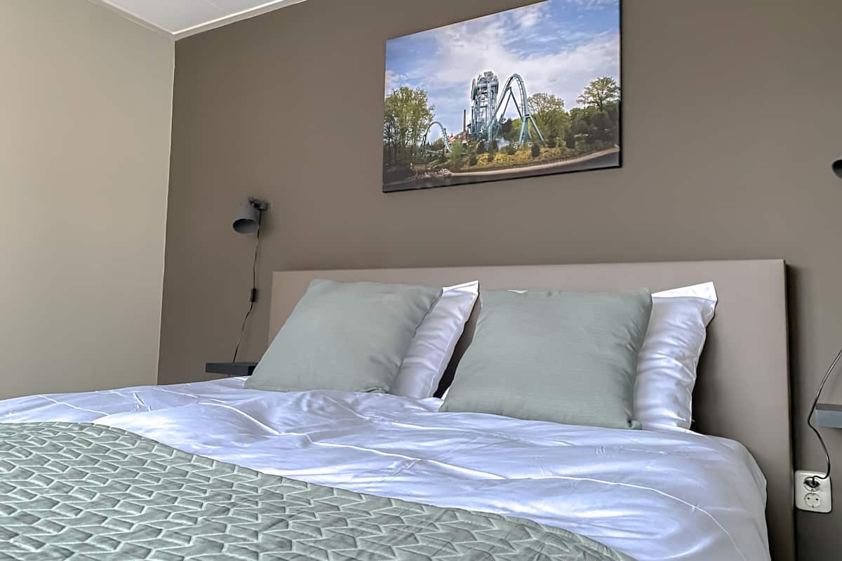 Un lit bien fait, avec une couvre-lit à motifs, une tête de lit et un tableau représentant des montagnes russes, accroché au mur.