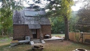 Ein rustikales Backsteinhaus mit Schornstein, einer kleinen Veranda und einem Grill.