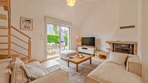 Amplia sala de estar con escalera de madera, televisor de pantalla plana, chimenea y un gran ventanal con vistas al exterior.