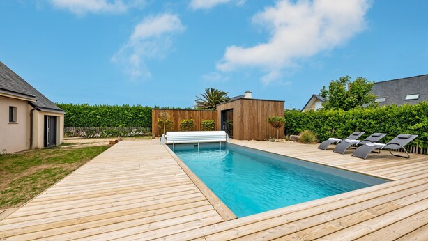 Una terraza de madera con piscina, sillas de descanso y un pequeño edificio de fachada de madera.