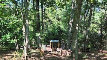 A forested area with a small wooden structure, possibly a shelter, surrounded by trees and a gravel path.