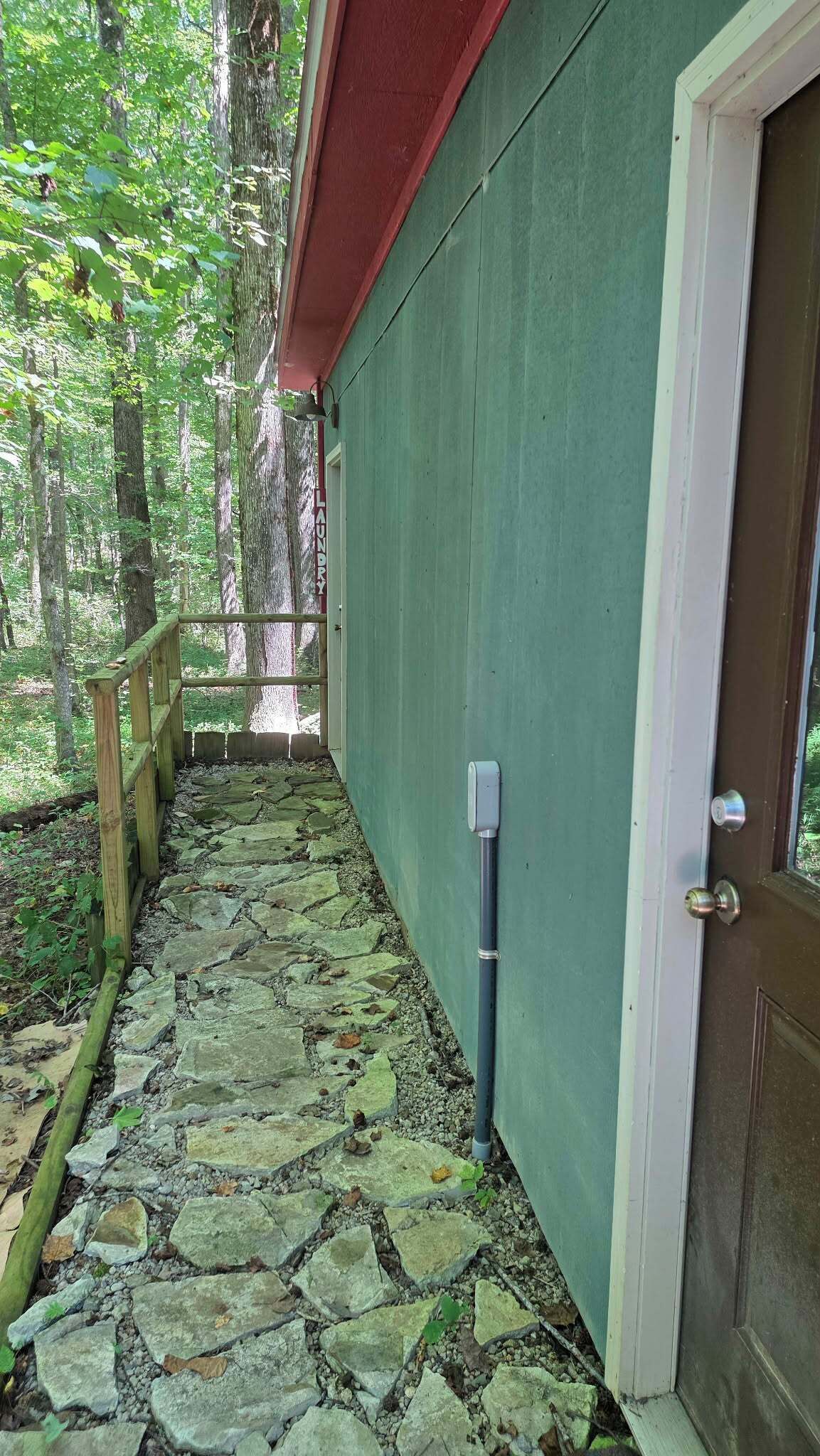 A stone pathway leading to a door with a metal pipe attached to the wall.