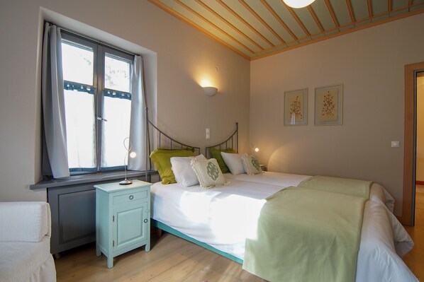 Une chambre à coucher comprenant un lit, une table de chevet, une fenêtre avec des rideaux et un luminaire fixé au mur.