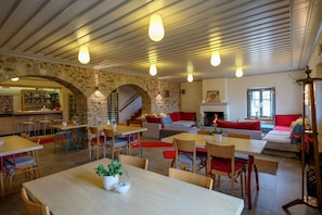 A spacious dining area with multiple tables and chairs, a stone archway, and a bar area in the background. - KIRIAKI GUESTHOUSE & SUITES (Amfikleia-Elateia)